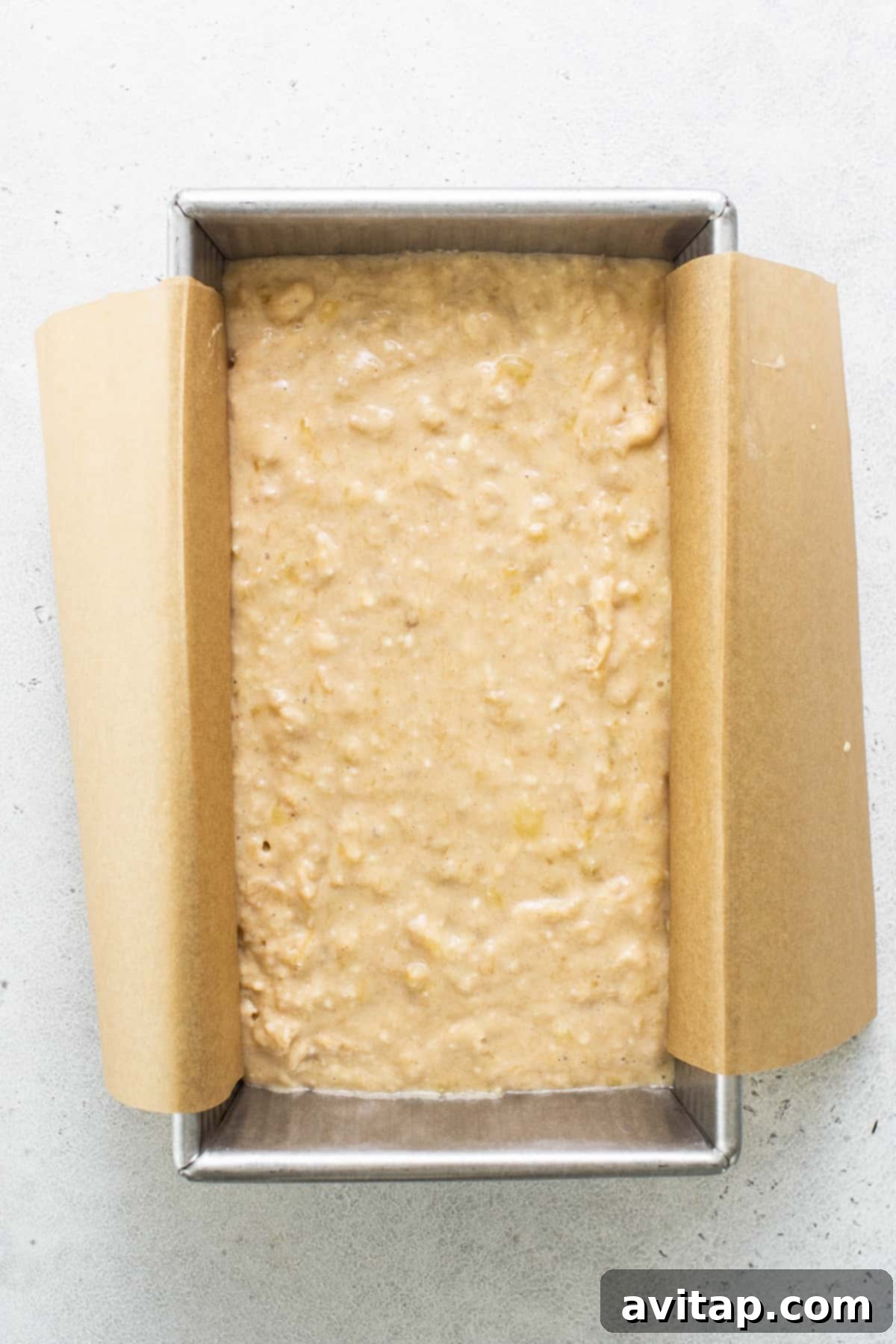 A freshly baked loaf of protein banana bread resting in a metal baking pan on a clean white surface.