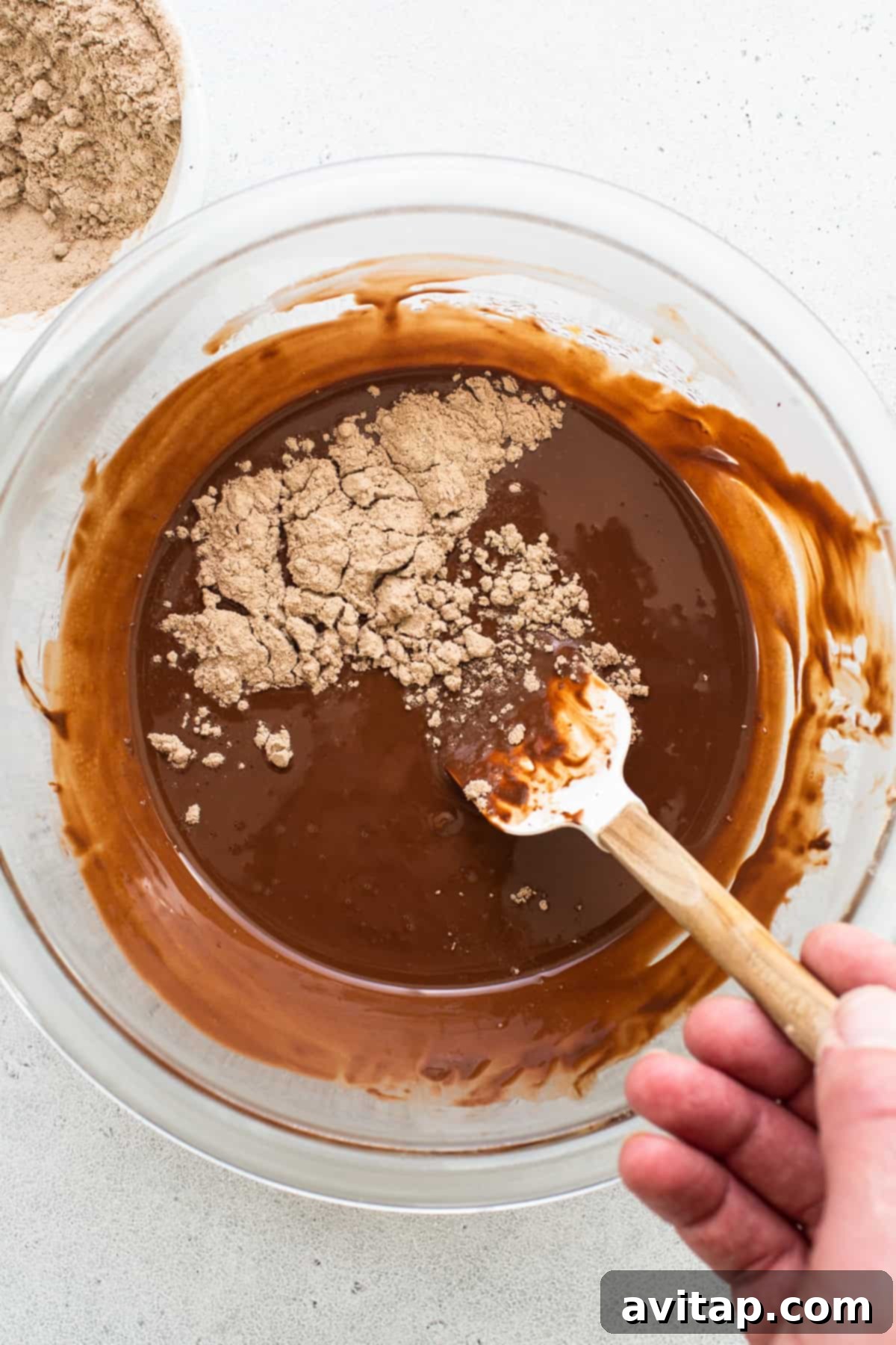 A person mixing chocolate in a bowl with a wooden spoon, ensuring a perfectly smooth and glossy consistency.
