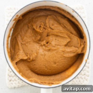 Peanut butter, honey, and coconut oil melting in a pan, stirred with a wooden spoon.