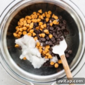 Chocolate and butterscotch chips in a bowl over a double boiler, being stirred with a wooden spoon.