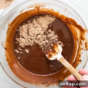 A person mixing chocolate protein powder into melted chocolate with a wooden spoon.