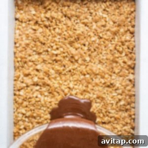 Rich chocolate sauce being poured and spread over the rice crispy base in a baking dish.