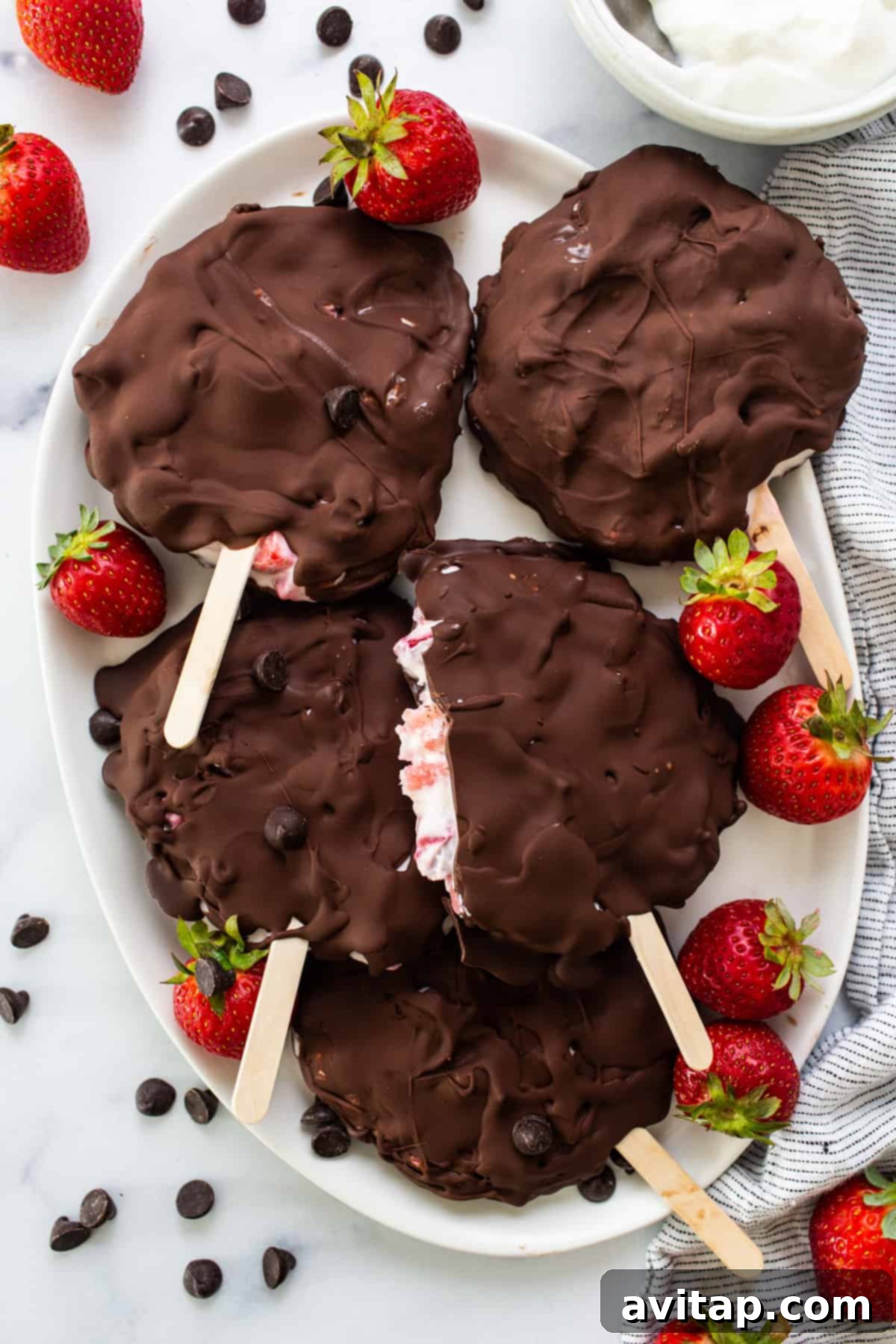 Two chocolate covered strawberry popsicles resting on a white plate, showcasing their inviting appearance and delicious appeal.