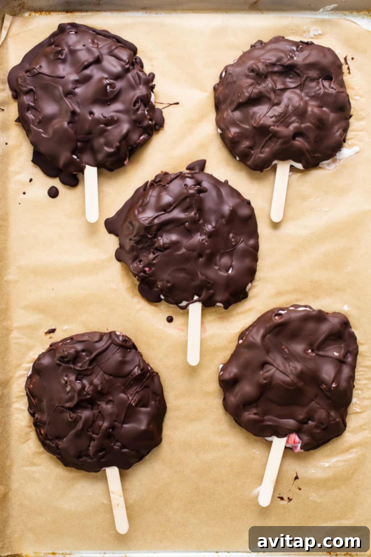 Finished chocolate covered frozen yogurt bars lined up on a parchment-lined baking sheet, showcasing their smooth chocolate coating after setting.