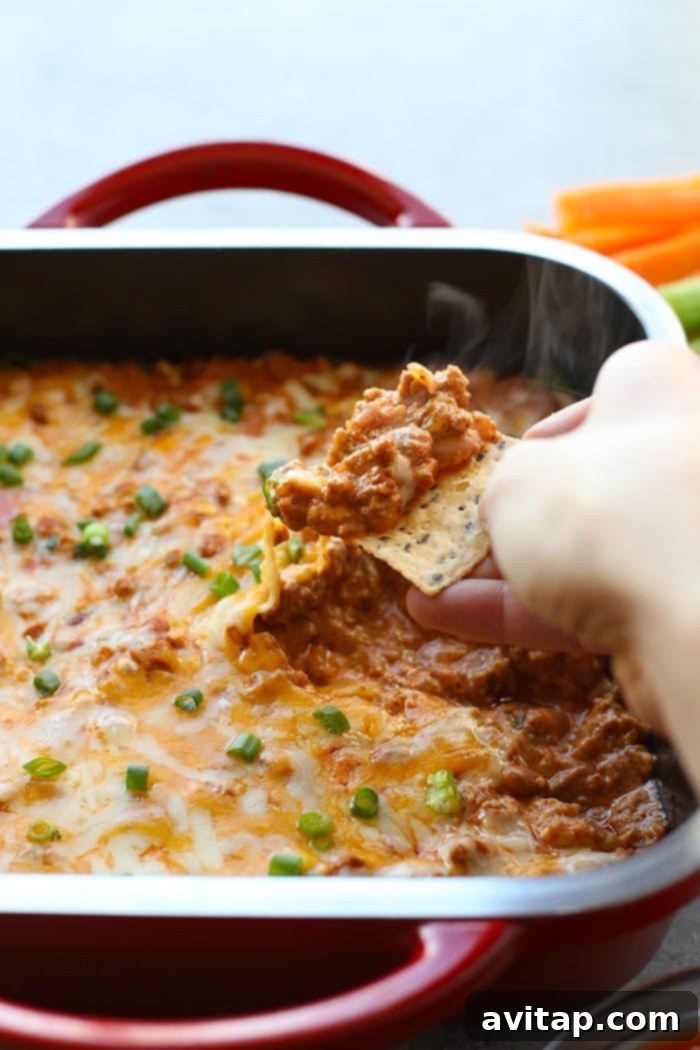Make this winning chili cheese dip for the big game and your guests will gobble it up. It really is the best chili cheese dip recipe! A chip being dipped into a bowl of warm chili cheese dip, showing the creamy texture and melted cheese.