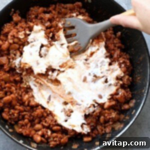 A person pouring cream into a frying pan to prepare a delicious chili cheese dip.