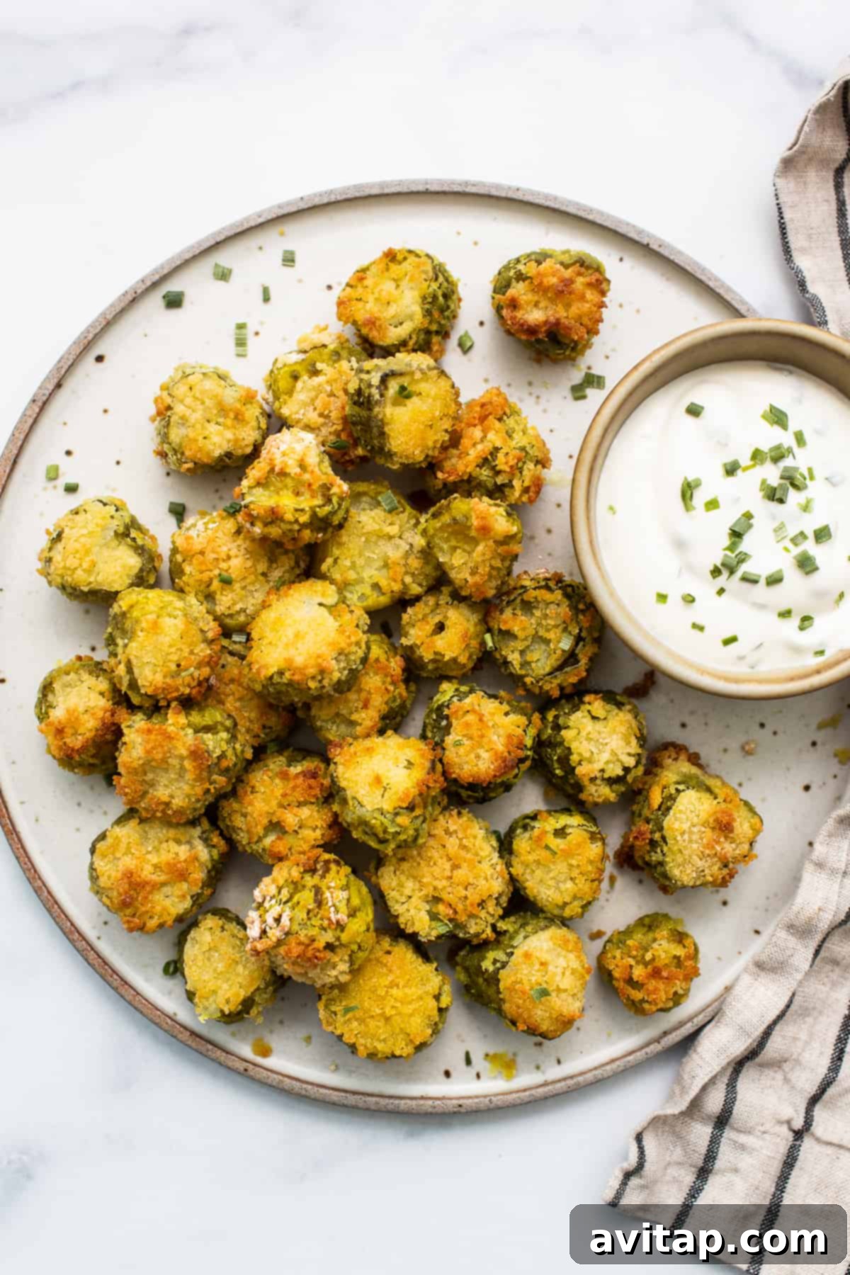 A plate of golden-brown air-fried pickles with a creamy dipping sauce on the side.
