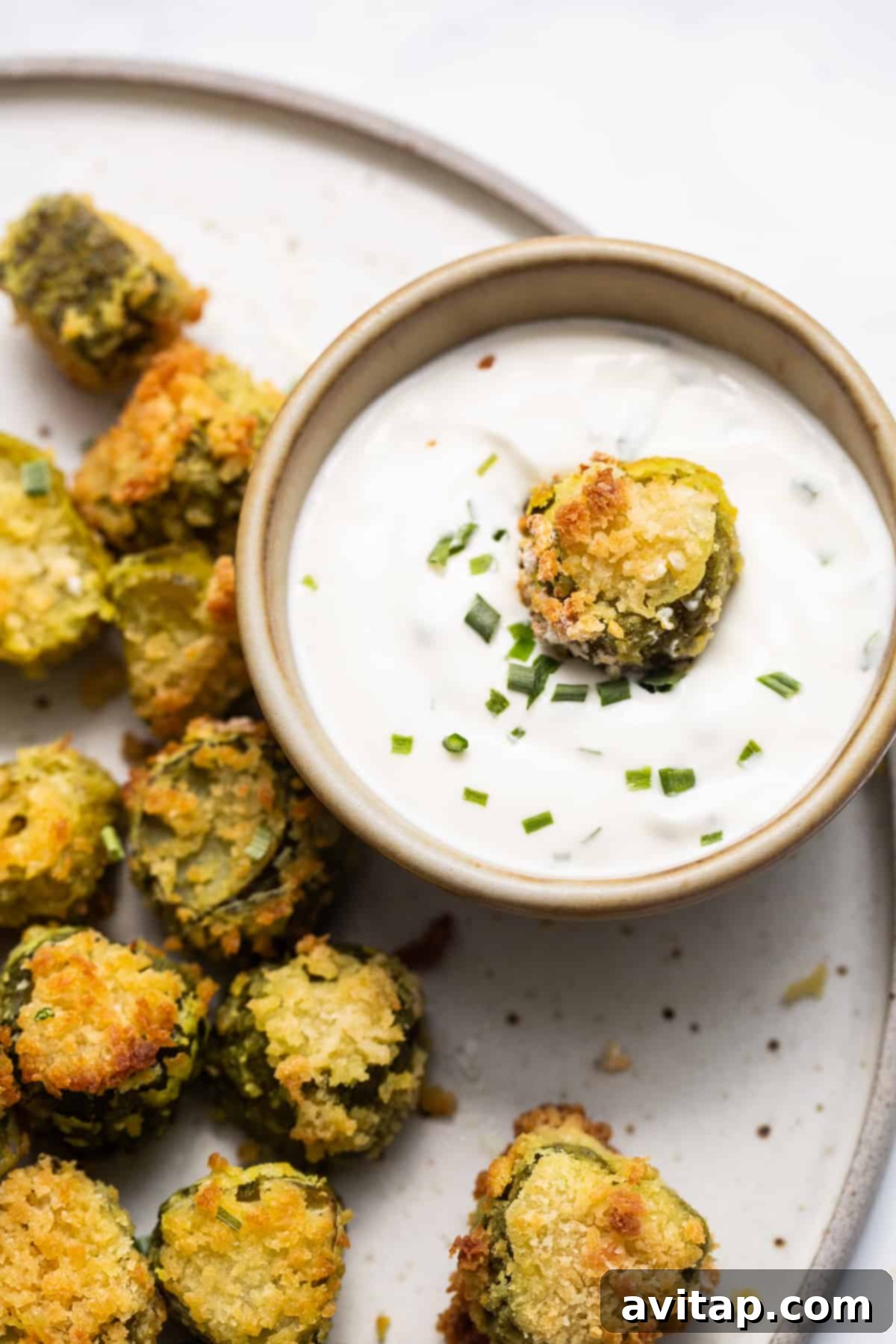 A vibrant plate of air-fried pickles served alongside a small bowl of creamy, zesty dipping sauce.