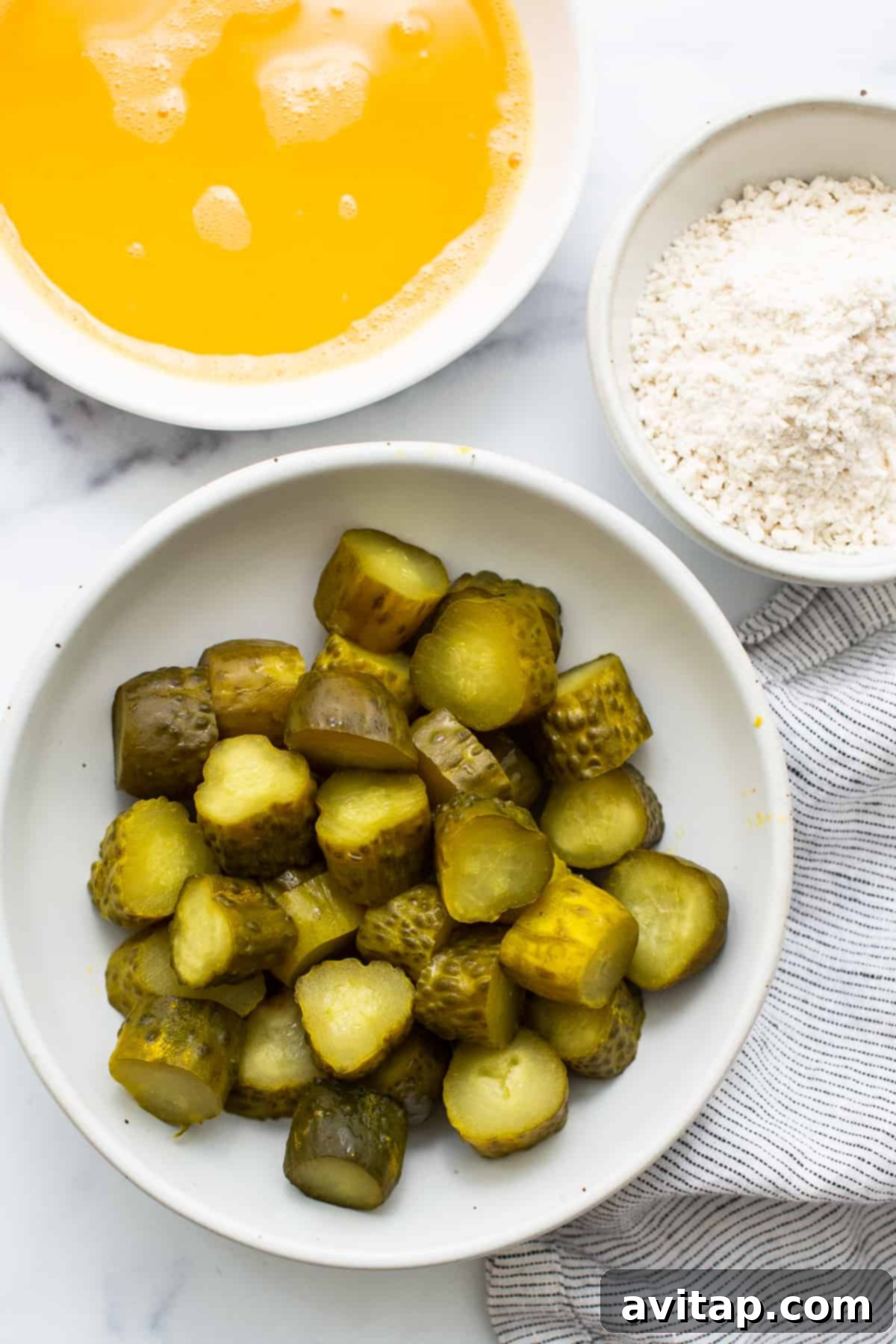A close-up shot of a bowl filled with sliced dill pickles next to a bowl of all-purpose flour, ready for breading.