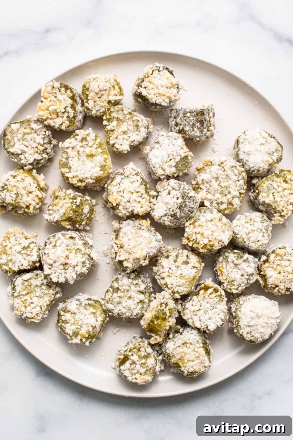 A close-up of beautifully golden-brown air-fried pickles arranged on a white serving plate, highlighting their crispy texture.