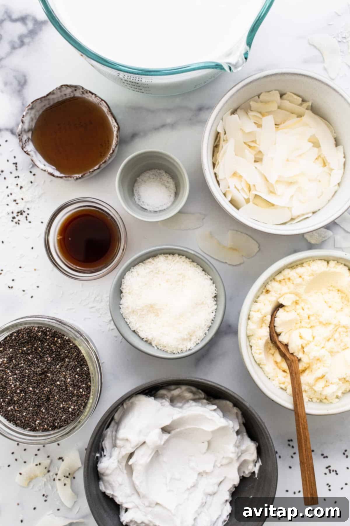 All the ingredients for coconut cream pie chia pudding laid out in bowls on a marble table, ready for preparation.