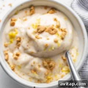 A bowl of creamy nice cream, topped with graham cracker crumbs and lemon zest, with a spoon.