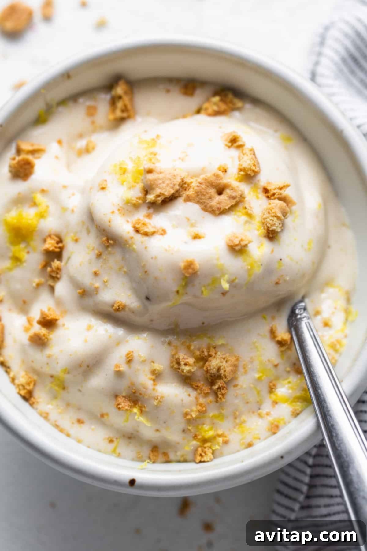 Zesty Lemon Cheesecake Nice Cream 6 A beautifully presented bowl of lemon cheesecake nice cream with graham cracker crumbs and lemon zest, with a spoon ready to scoop.