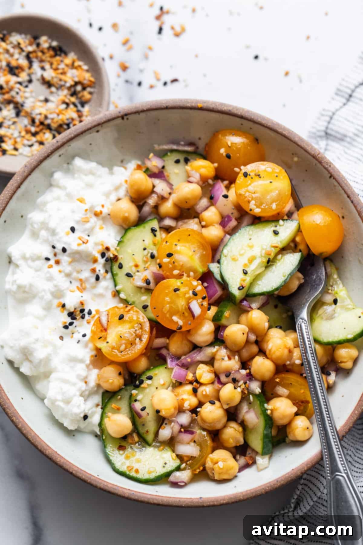 A vibrant bowl featuring golden chickpeas, crisp green cucumber slices, and fluffy white cottage cheese, ready to be enjoyed.