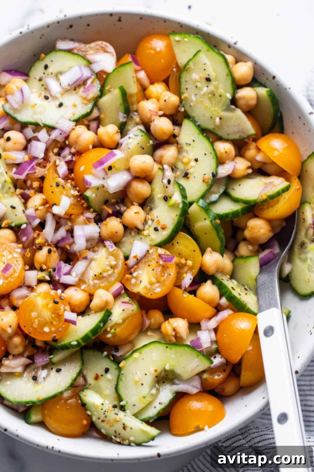 A vibrant bowl of chickpea and cucumber salad, perfectly tossed and dressed, with a spoon ready for serving.