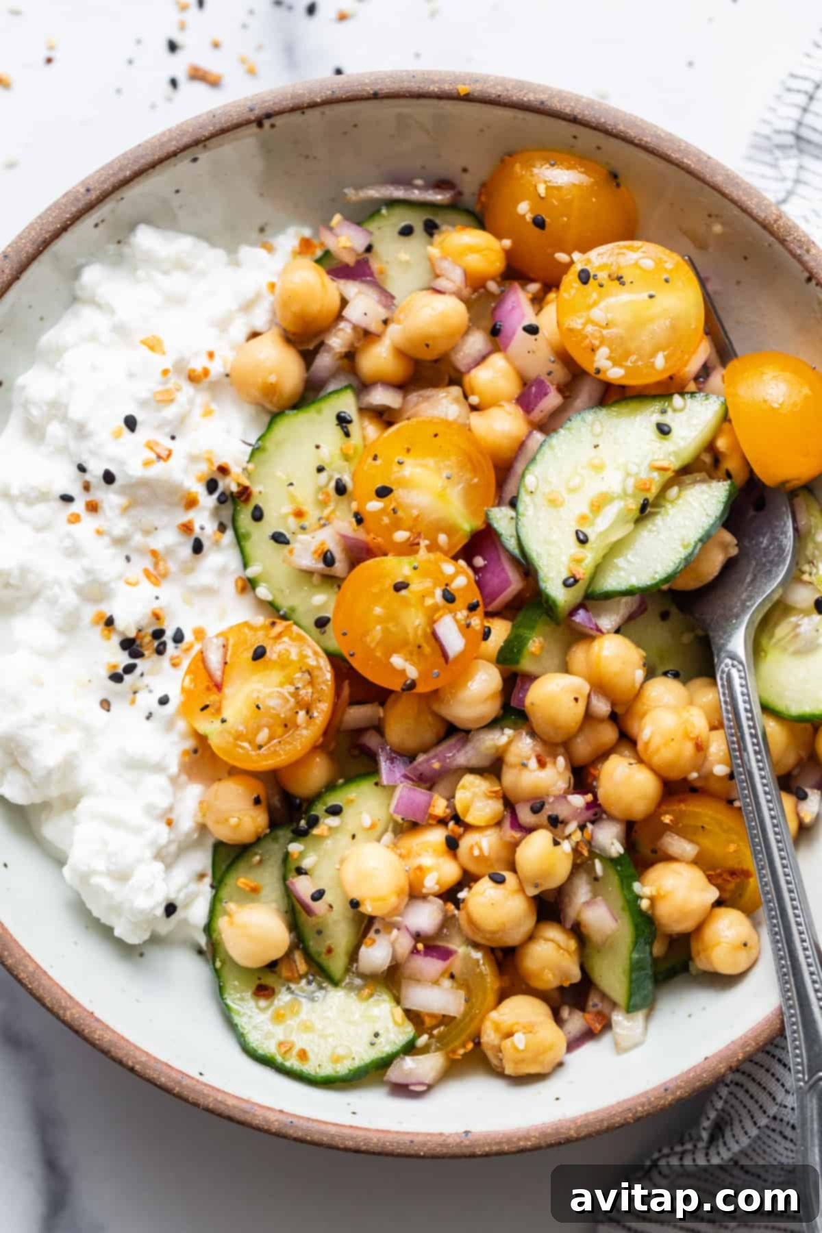 A close-up of a bowl filled with vibrant chickpeas, sliced cucumbers, and a creamy base of cottage cheese, highlighting the fresh textures.
