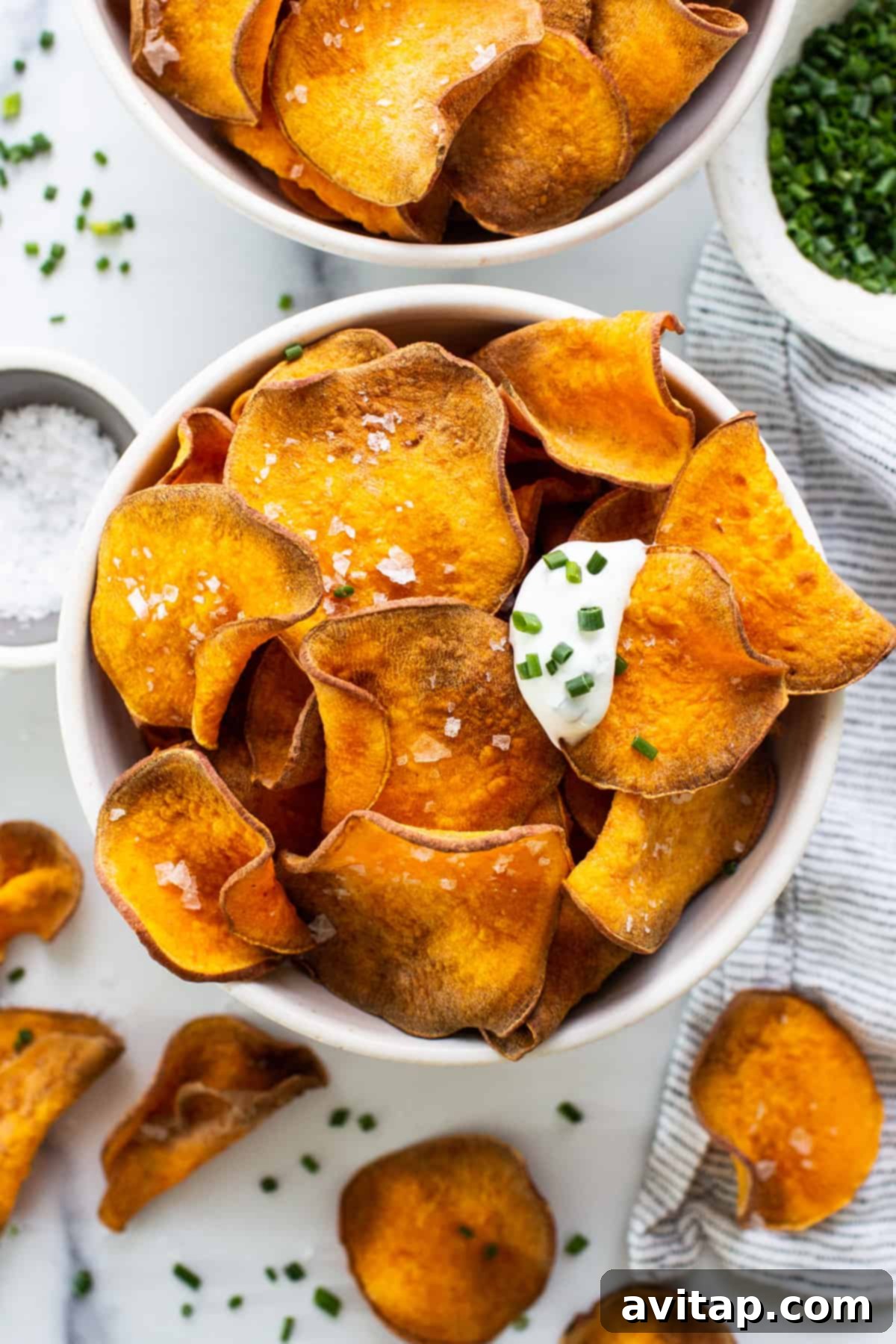 Crispy air fryer sweet potato chips served with a side of sour cream and fresh chives, garnished beautifully.