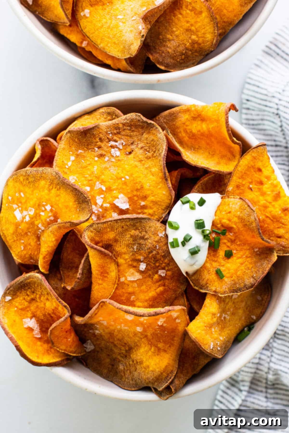 Two bowls brimming with golden sweet potato chips, garnished with fresh sour cream and chives.