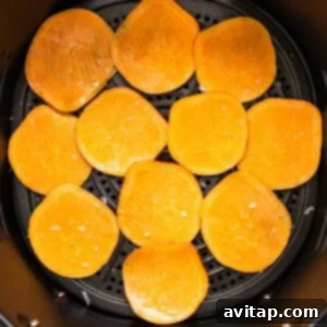 Thinly sliced sweet potato chips arranged in an air fryer basket, ready for cooking.