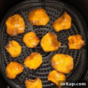 A close-up view of various thin slices of sweet potato being cooked to perfection inside an air fryer basket.