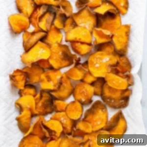 Golden-brown sweet potato chips spread out on a paper towel-lined baking sheet to cool.