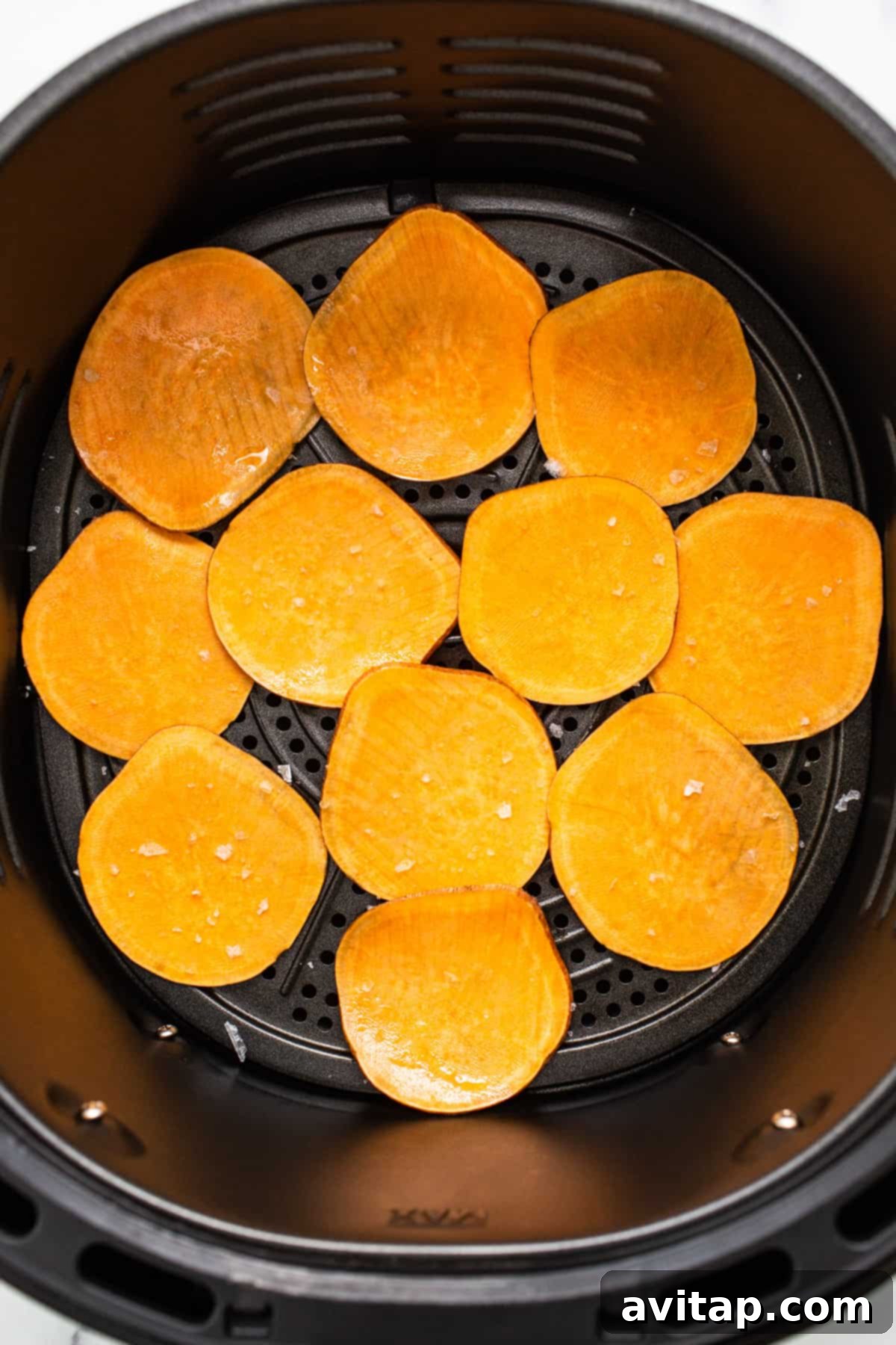 Thinly sliced sweet potato chips arranged in an air fryer basket, ready for cooking.