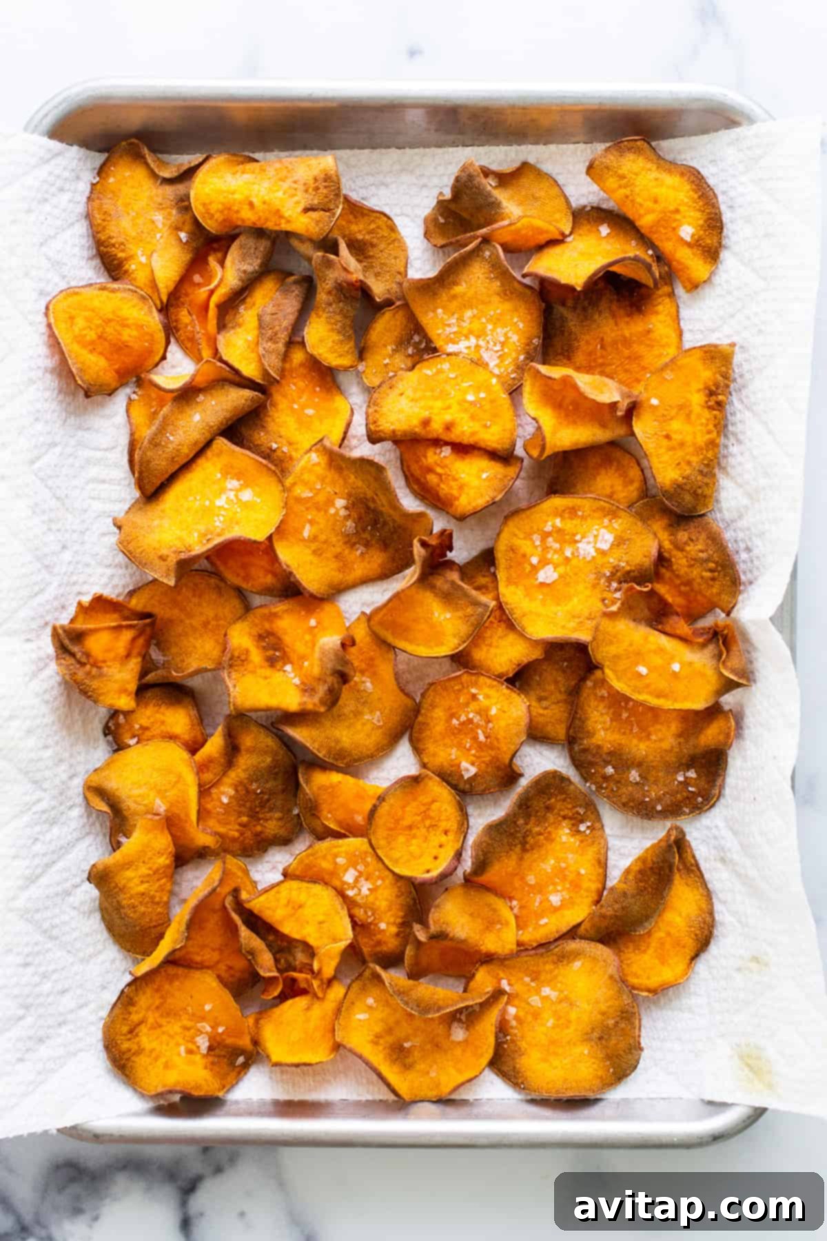Golden-brown sweet potato chips spread out on a paper towel-lined baking sheet to cool.
