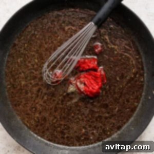A frying pan with a rich red sauce being stirred, incorporating a red pepper.