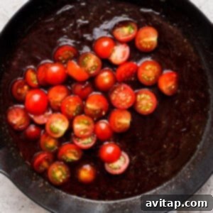 A frying pan with cherry tomatoes and simmering sauce, before the chicken is added back.
