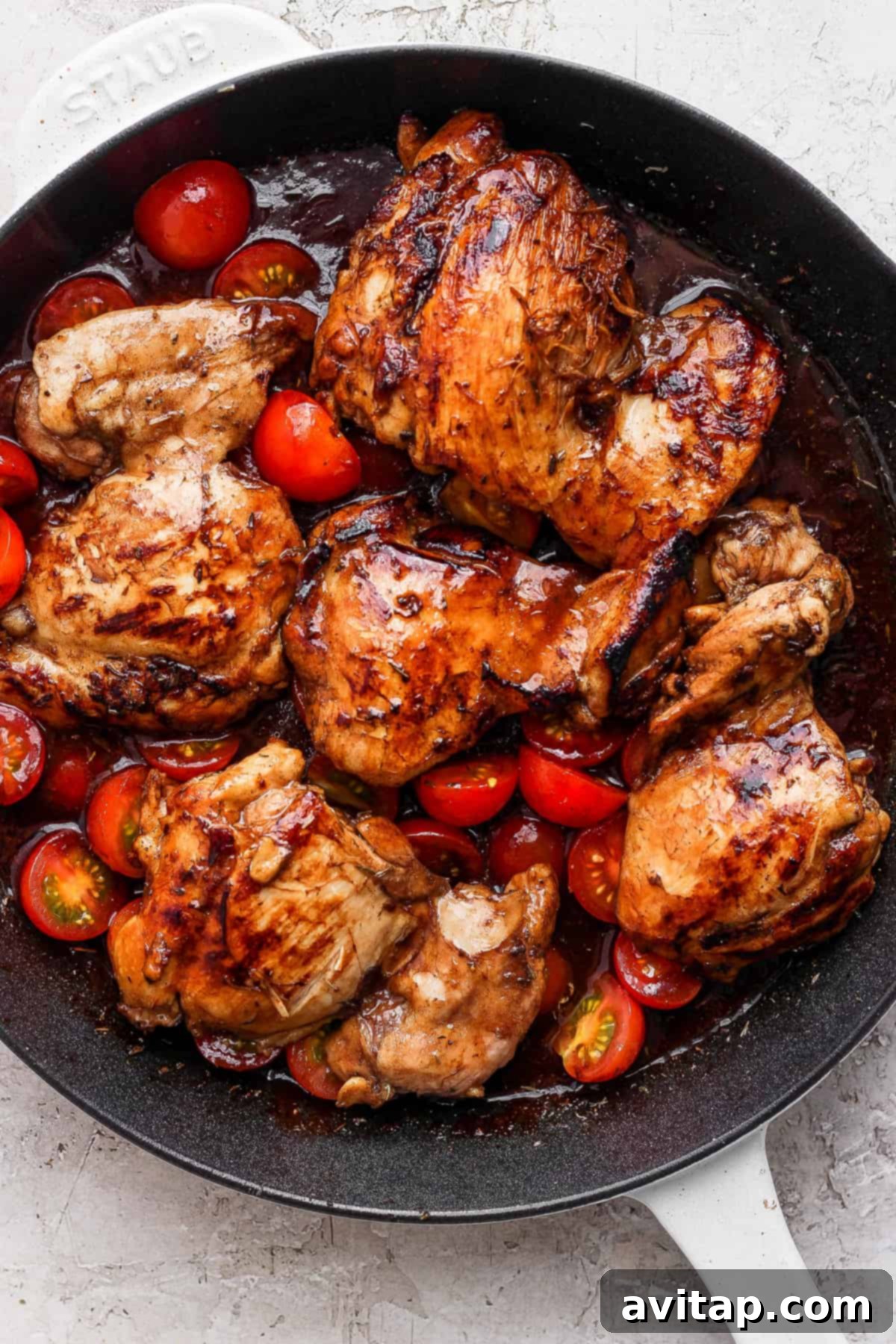 Close-up of seared chicken thighs simmering in a rich tomato and balsamic sauce with halved cherry tomatoes in a cast iron skillet.