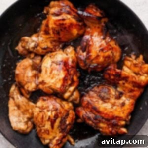 Close-up of juicy grilled chicken in a skillet, showcasing its golden-brown exterior, on a white background.