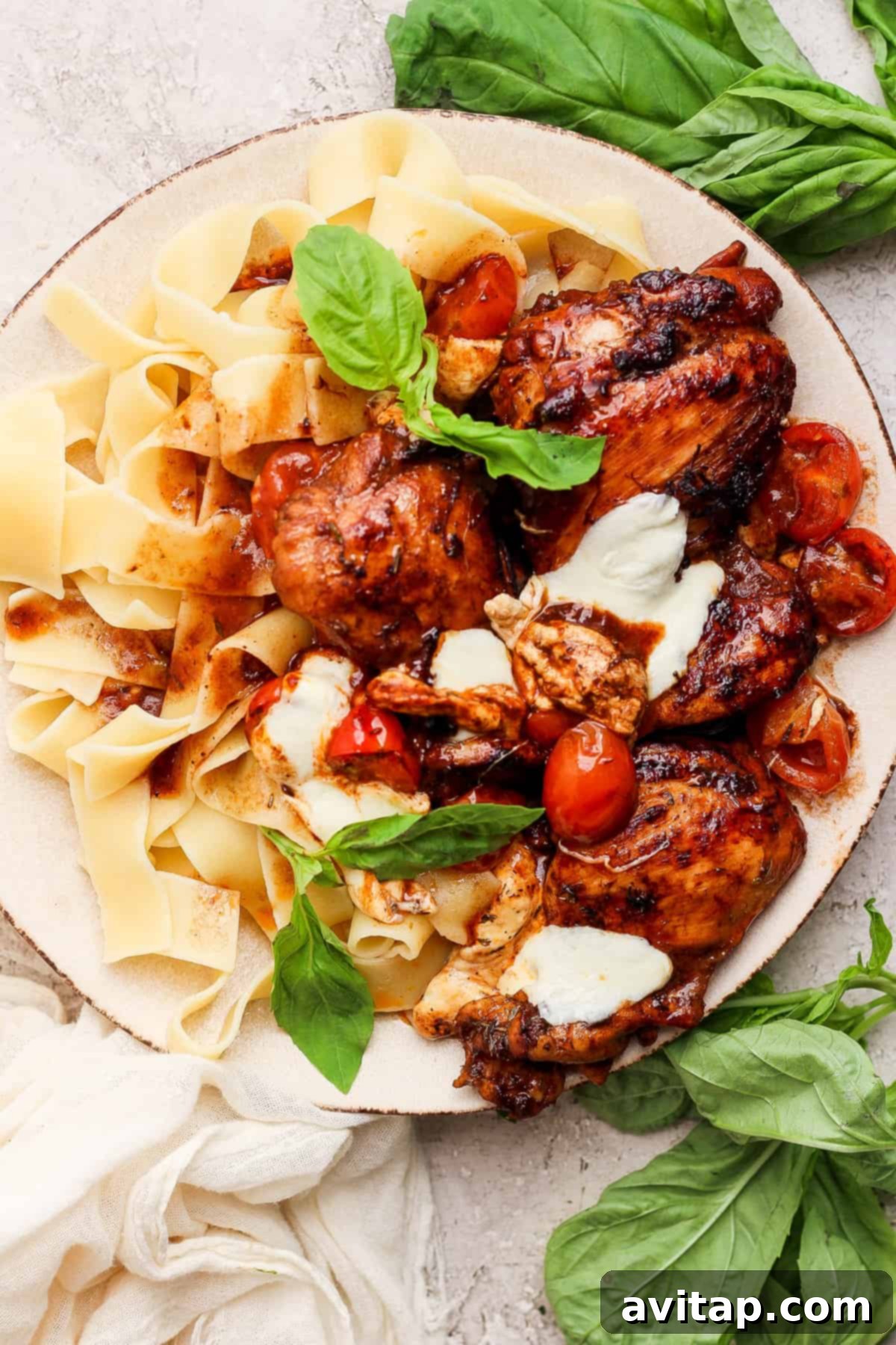 A beautifully plated dish of pappardelle pasta topped with balsamic chicken thighs, cherry tomatoes, and fresh basil.