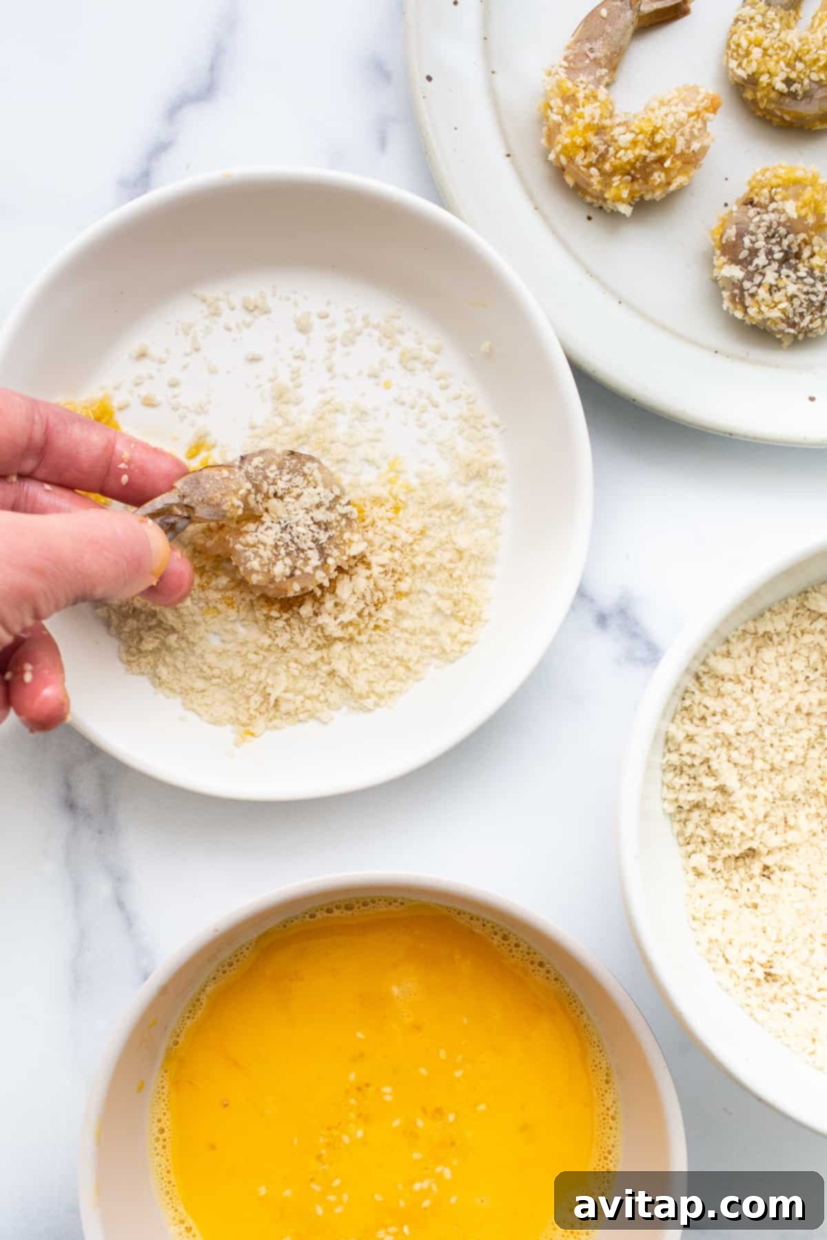 A person drizzling white sesame seeds into a bowl of ingredients for firecracker shrimp sauce.