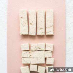 Tofu cubes coated in cornstarch on a pink cutting board, ready for frying.