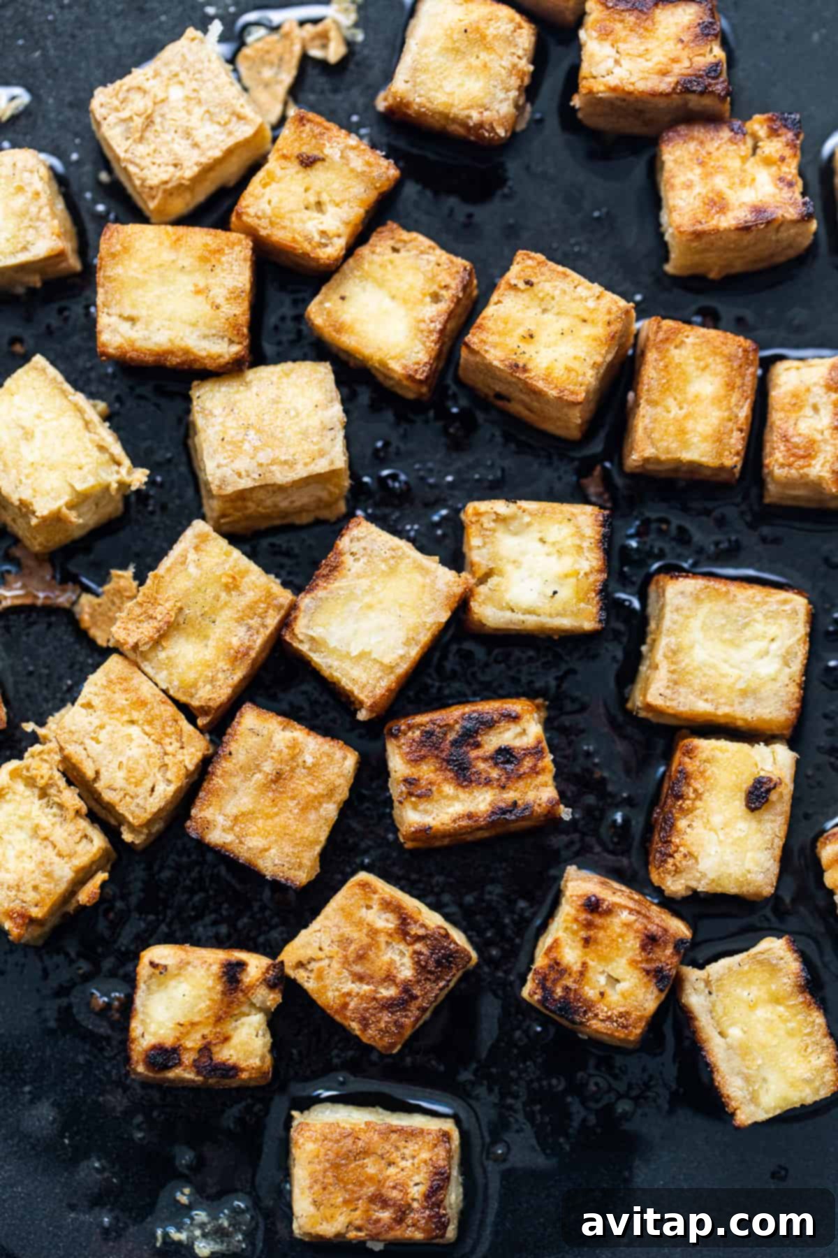 Close-up of tofu cubes being pan-fried to a golden crisp in a hot skillet.
