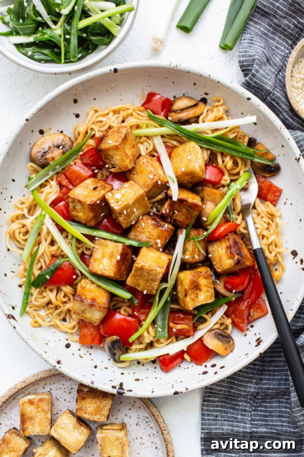 A serving of Crispy Tofu Stir Fry in a white plate, showcasing a mix of noodles, vegetables, and golden tofu.
