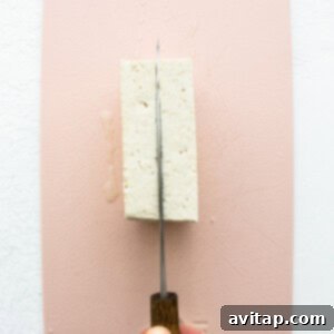 A person cutting a piece of tofu on a pink surface before pressing.