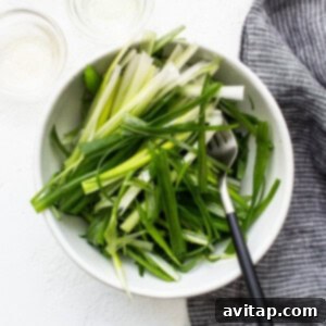 A white bowl filled with freshly prepared green onion salad and a fork.