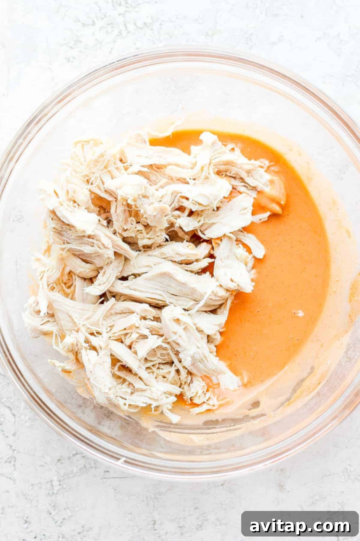 Shredded chicken generously coated in vibrant buffalo sauce, sitting in a mixing bowl ready for wrap assembly