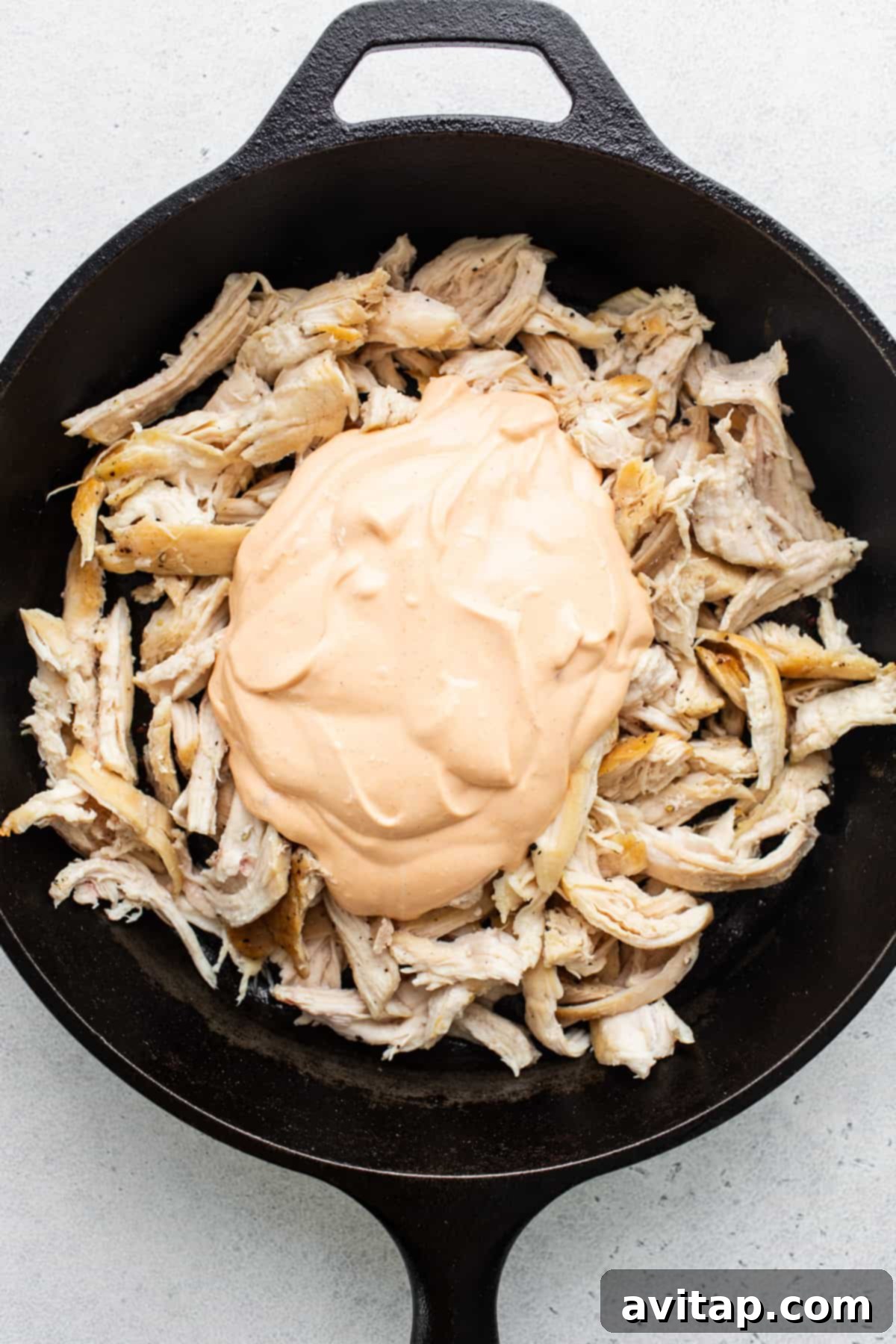 Cooked shredded chicken coated in creamy buffalo sauce in a skillet, before adding cheese and baking.