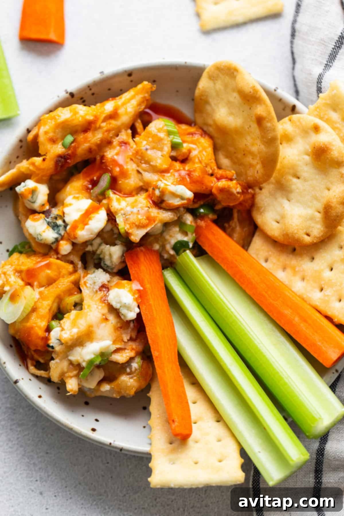 A charming table spread with a bowl of hot whipped cottage cheese buffalo chicken dip, surrounded by an assortment of dippers including celery sticks, carrot sticks, and various crackers.
