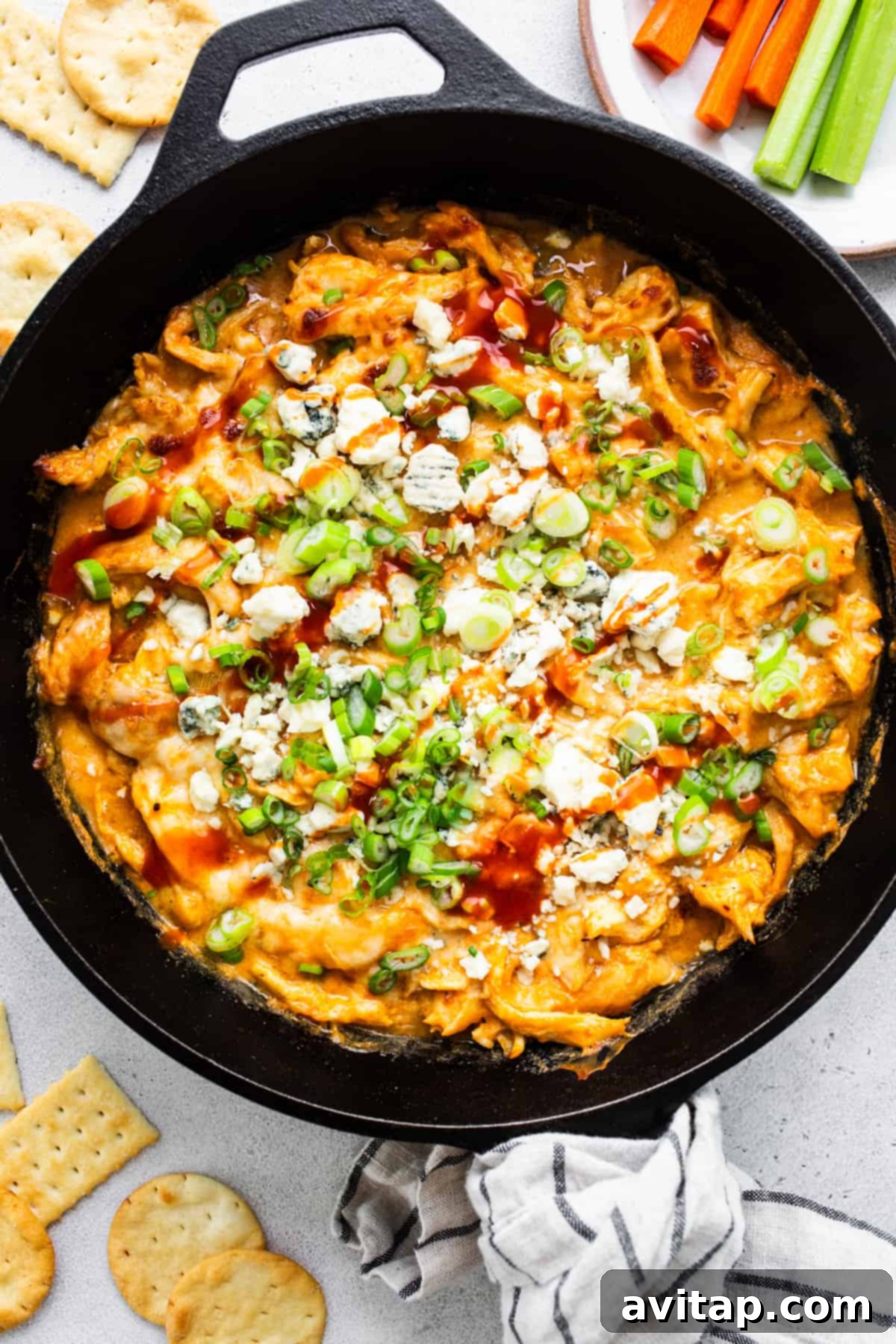 A close-up shot of a hot, cheesy, bubbly buffalo chicken dip in a rustic skillet, with crispy crackers artfully arranged on the side, ready to be devoured.