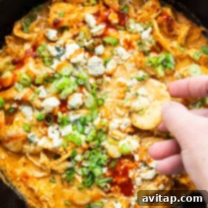 A close-up of a serving of buffalo chicken dip with a chip, showing its creamy texture and fresh green onion garnish.