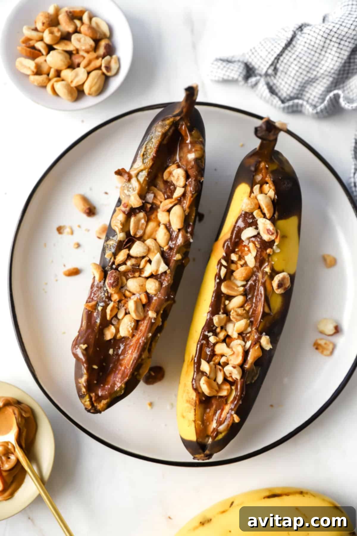 Two air-fried bananas with melted peanut butter, chocolate, and chopped peanuts on a plate.
