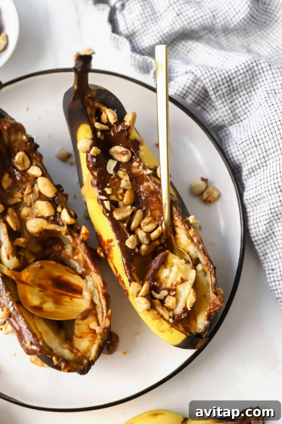 Two air-fried bananas stuffed with peanut butter and chocolate, topped with chopped peanuts on a white plate.