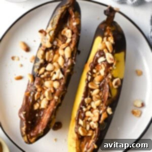 Two air-fried bananas with melted peanut butter and chocolate on a plate, topped with chopped peanuts.