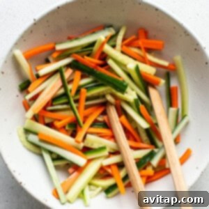 A white bowl with carrots and cucumbers in it.