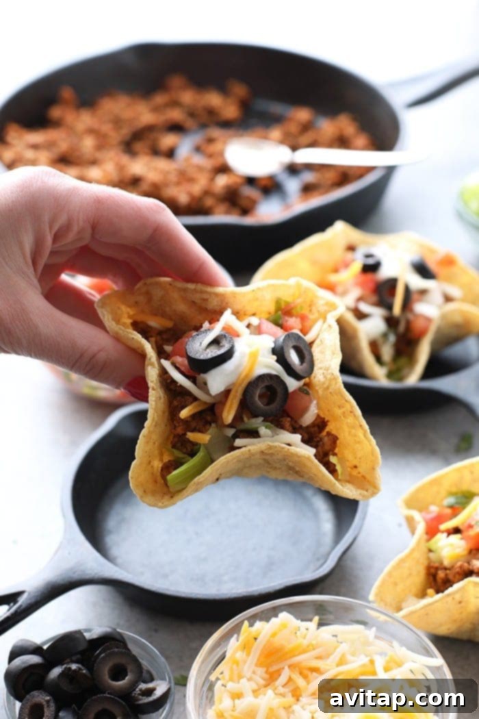 A hand presenting a perfectly assembled mini baked taco cup, highlighting its irresistible appeal and vibrant colors.