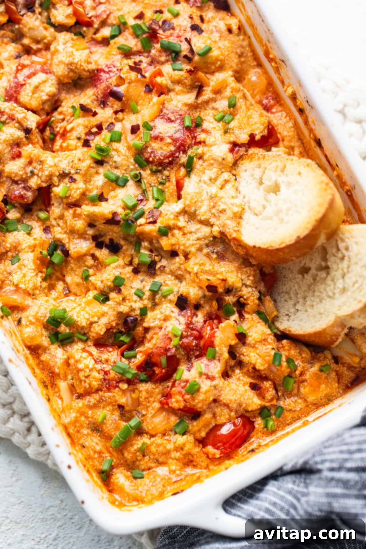 Creamy Roasted Garlic Boursin Bake 2 A casserole dish with golden-brown baked Boursin dip, roasted tomatoes, and garlic cloves, served with crusty bread.