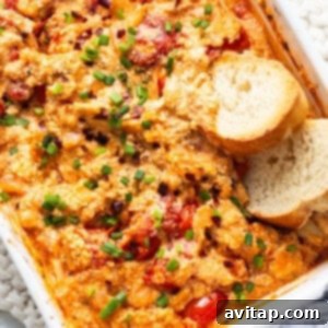 A casserole dish with golden-brown baked Boursin dip, roasted tomatoes, and garlic cloves, served with crusty bread.